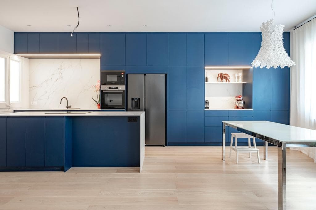Cocina abierta con encimera Calacatta e isla entre frentes azules